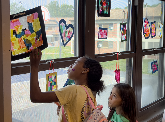 Two kids at a window with paintings